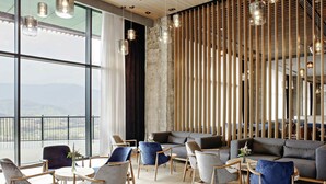 Eine moderne Lounge mit Blick auf die Landschaft, ausgestattet mit einer Mischung aus Sofas und Sesseln, Holzakzenten und hängenden Pendelleuchten.