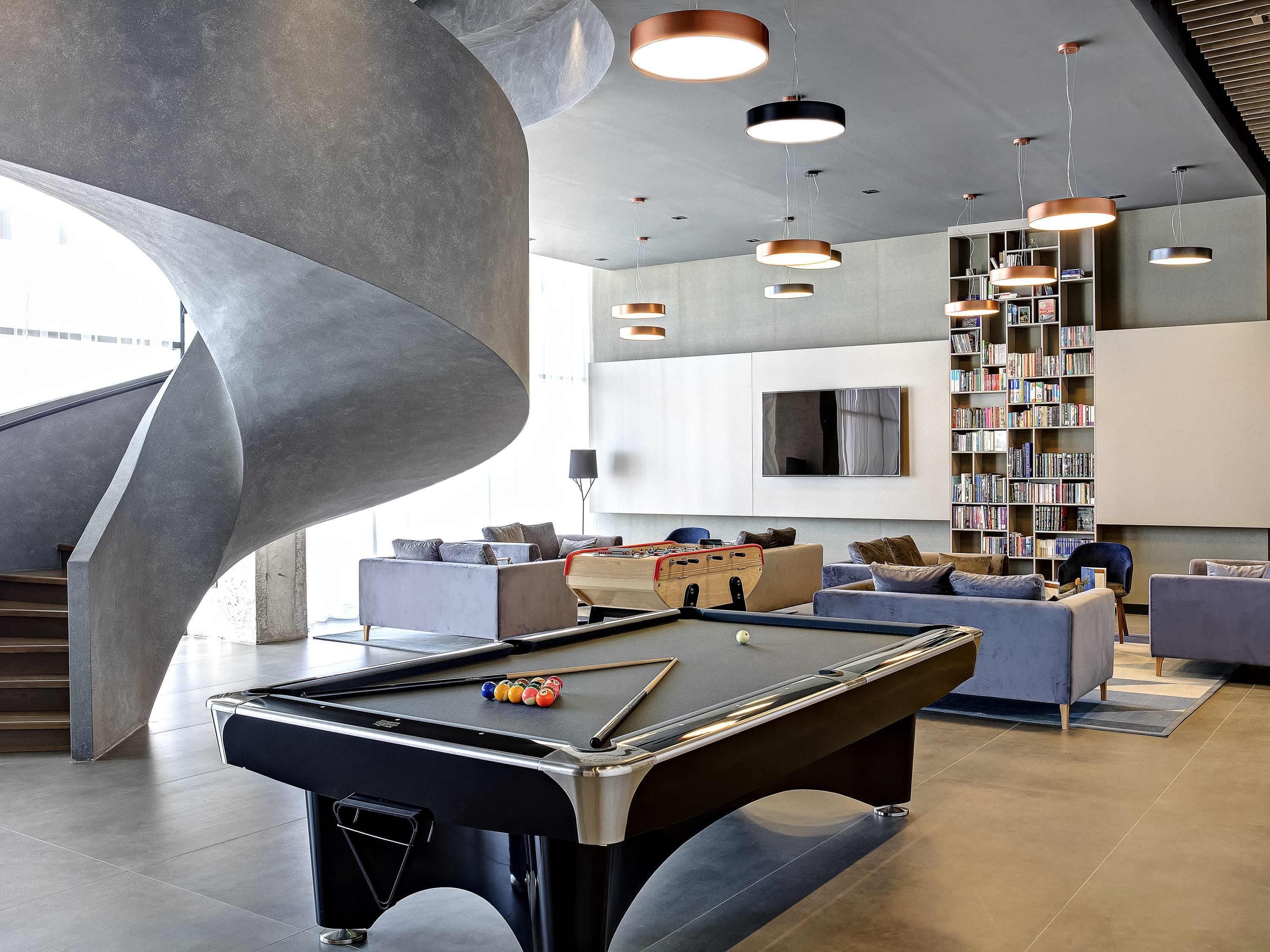 A modern lounge area with a pool table, sofas, a bookshelf, and a large abstract sculpture.