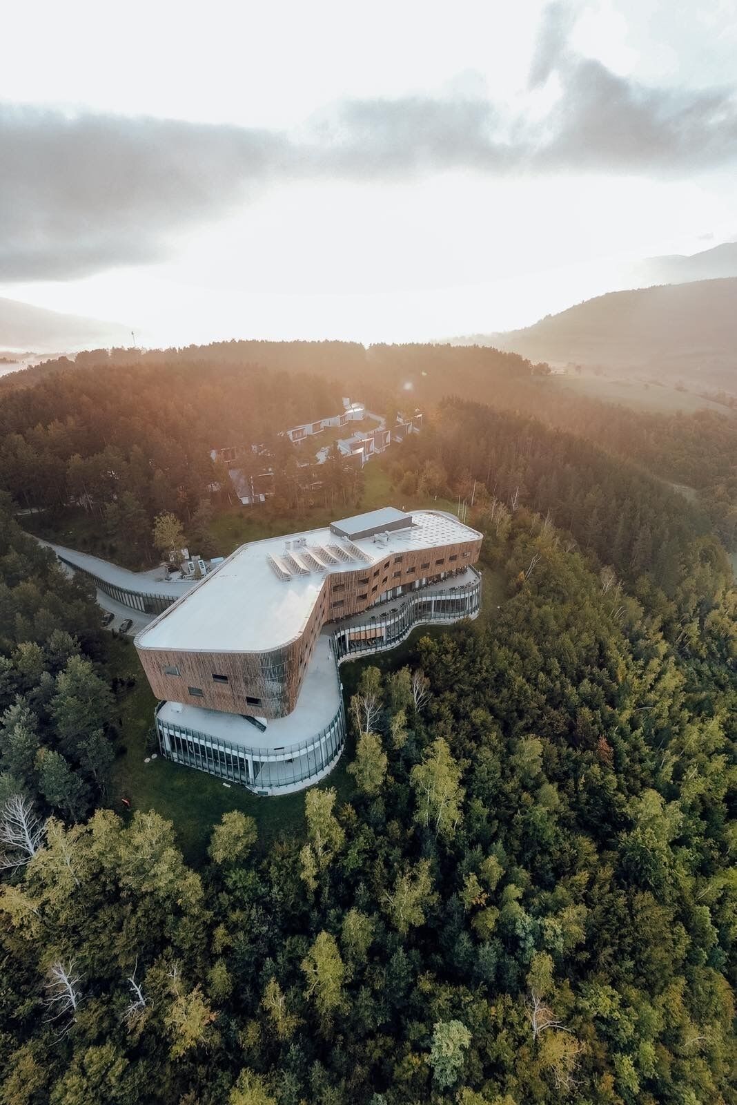 A modern building with a unique curved roof, surrounded by dense forest.