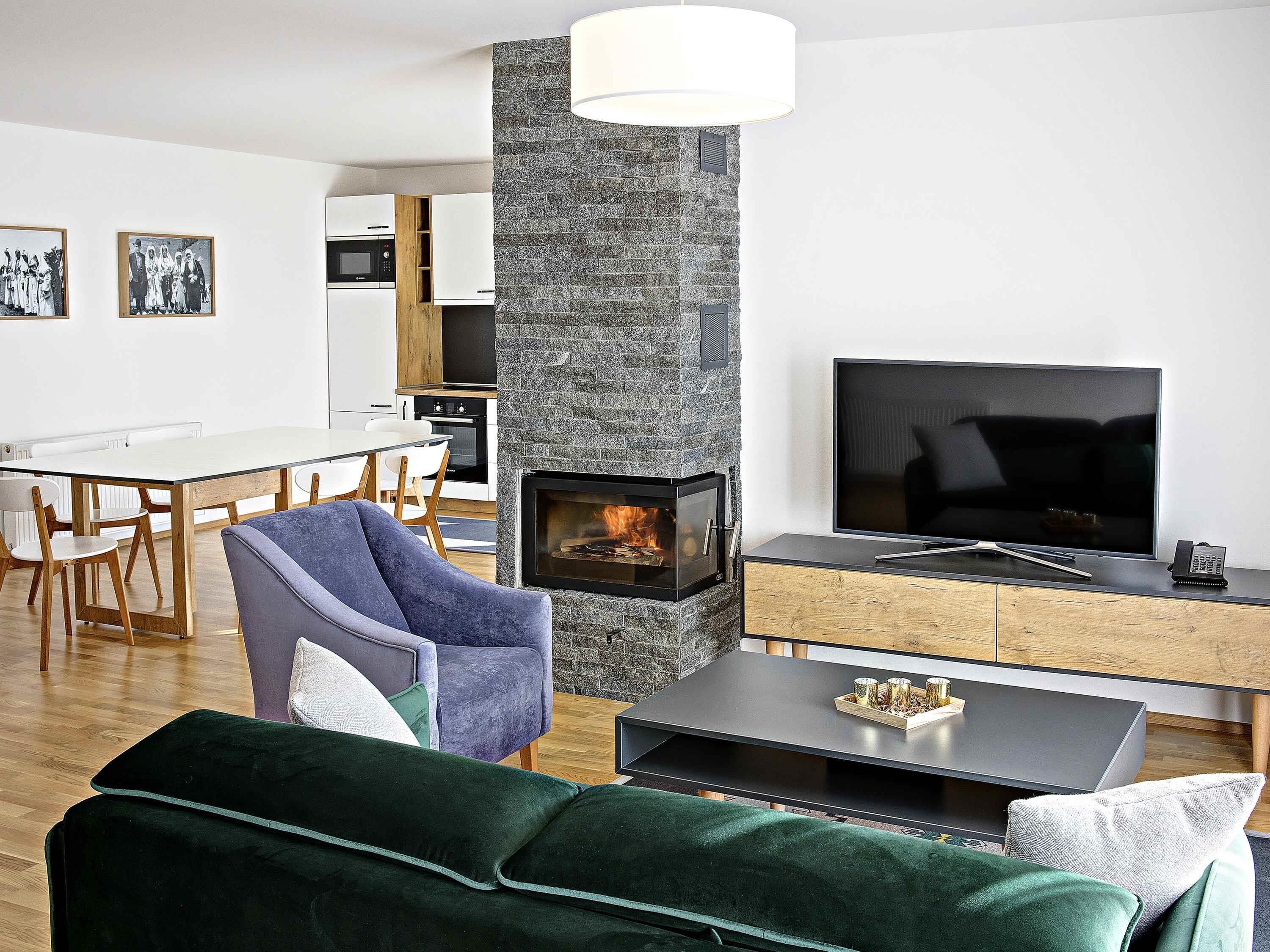 A modern living room with a stone fireplace, a flat-screen TV, and a dining area in the background.