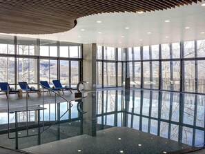 Ein modernes Hallenbad mit Glaswänden, blauen Liegestühlen und freiem Blick ins Freie.