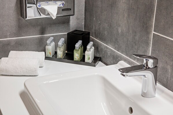 Ein Badezimmer mit weißem Waschbecken, Armatur aus Chrom und Spender für Handtücher.