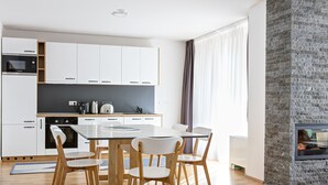 A modern kitchen with white cabinets, a built-in oven, and a dining area with a glass table and wooden chairs. - Tarcin Forest Resort & Spa Sarajevo - MGallery Collection (Resnik)