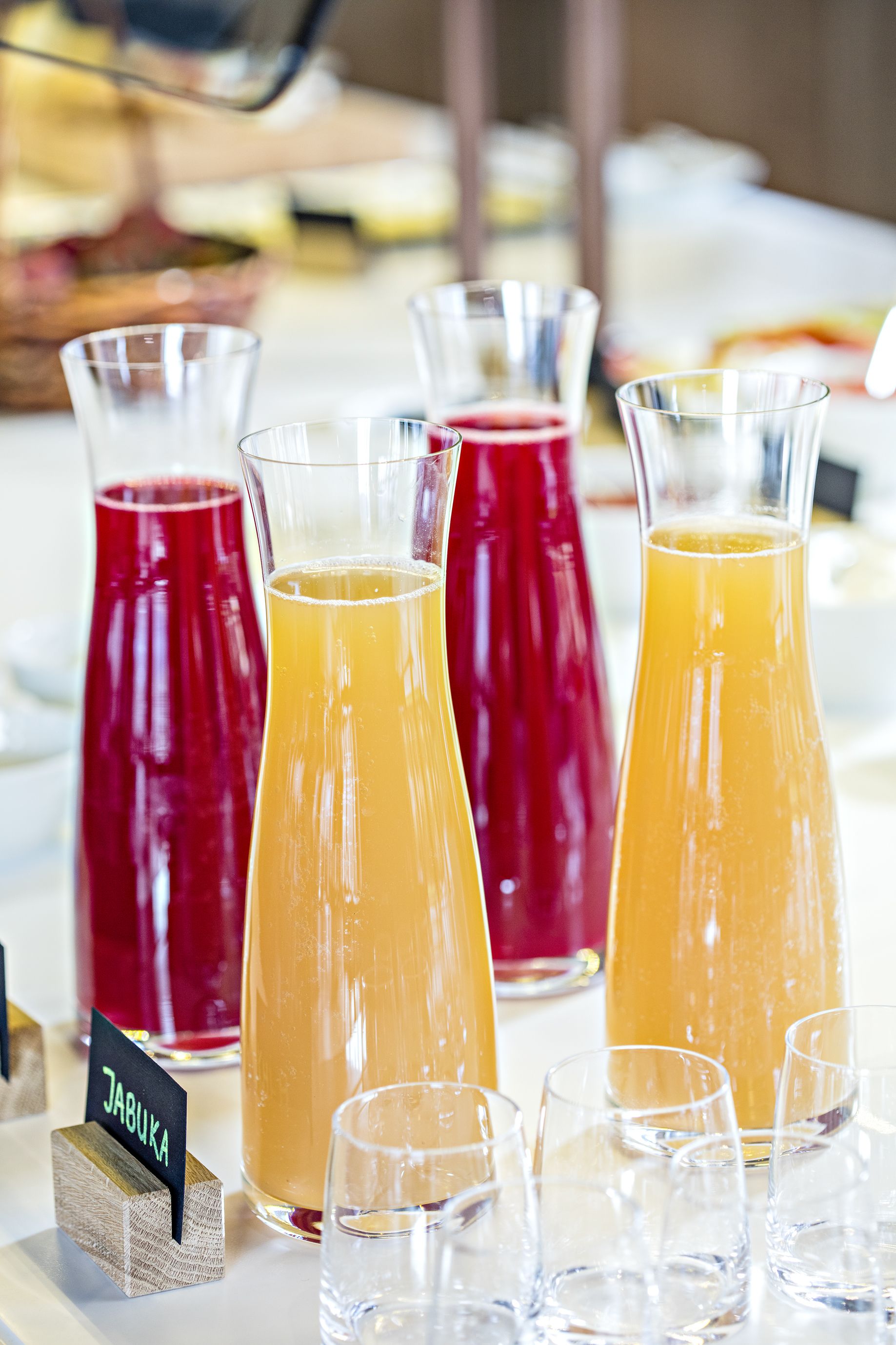 Una mesa con varios jarras de bebidas, algunas etiquetadas, y vasos vacíos al frente.