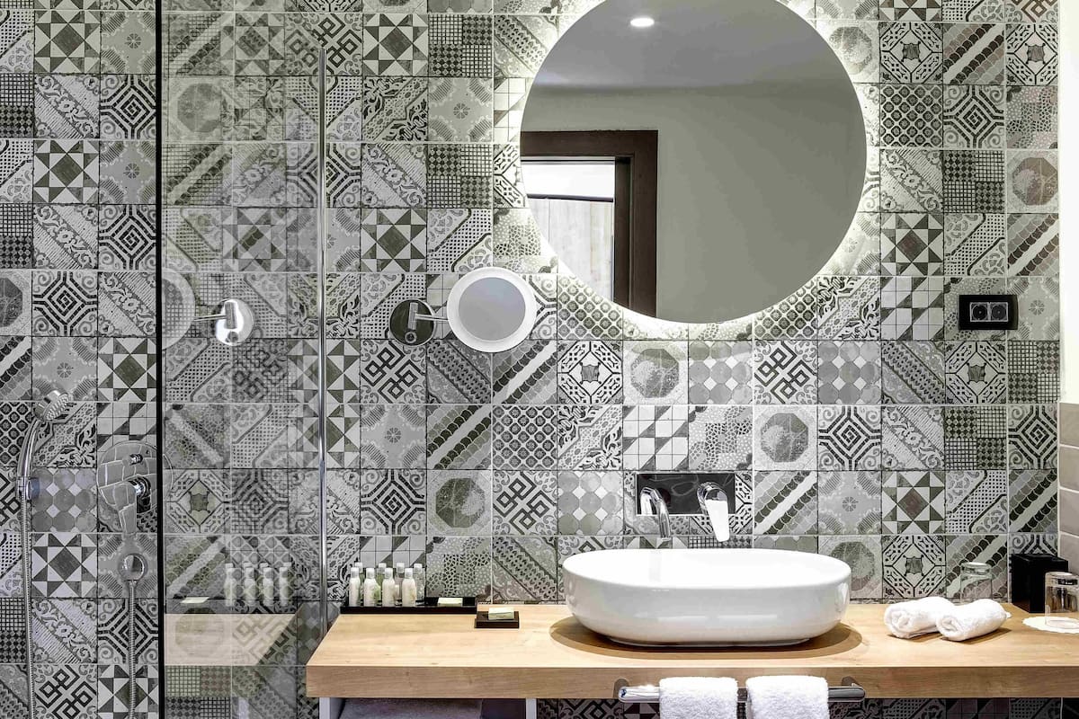 Un baño con espejo redondo, lavamanos y azulejos estampados.
