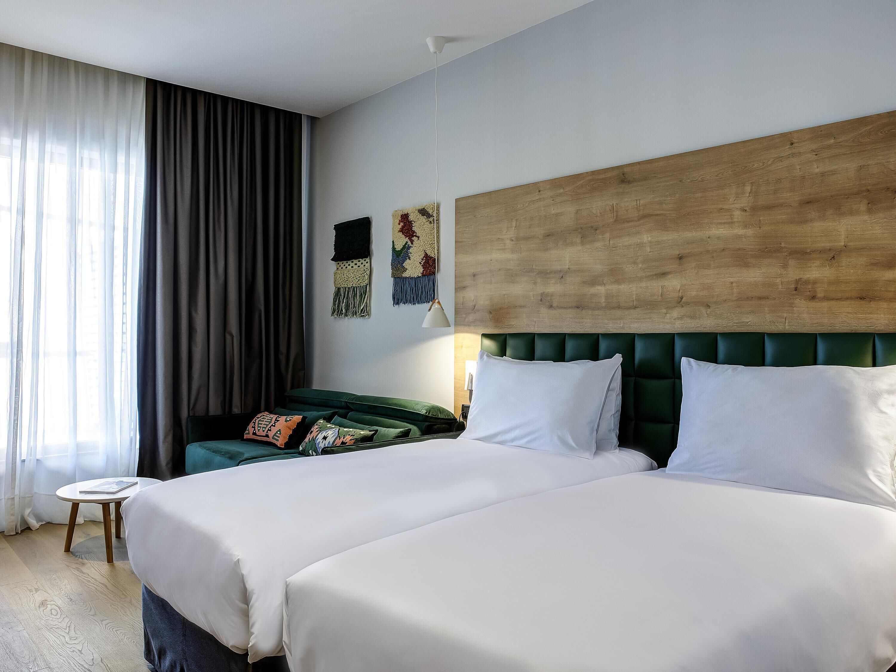 Une chambre d’hôtel avec deux lits, une tête de lit en bois, une petite table ronde et une vue sur l’extérieur.