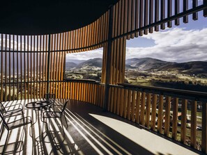 A balcony with a view of a valley, wooden slats, and a table with chairs.