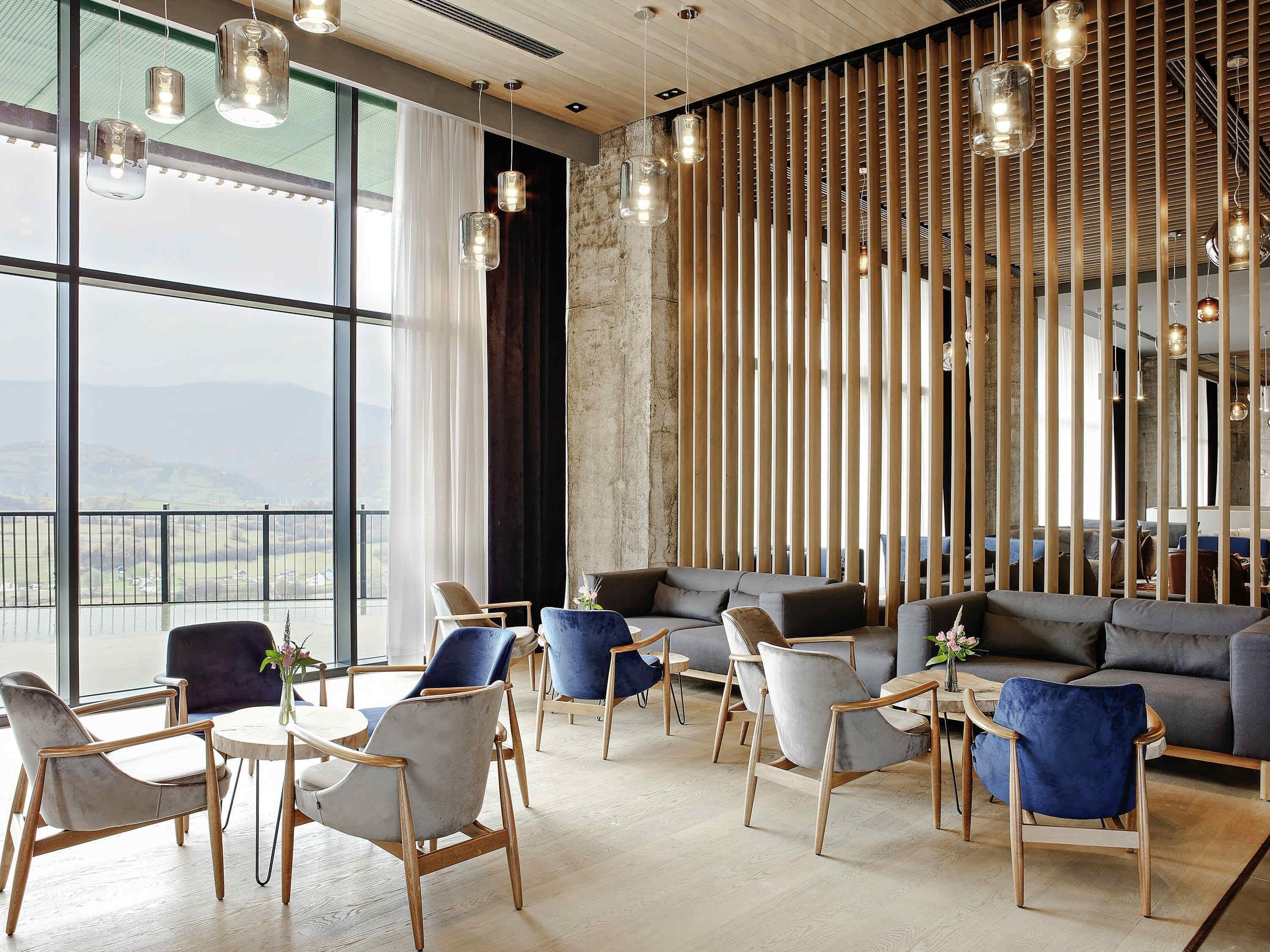 A modern lounge with a view of the countryside, featuring a mix of sofas and chairs, wooden accents, and hanging pendant lights.