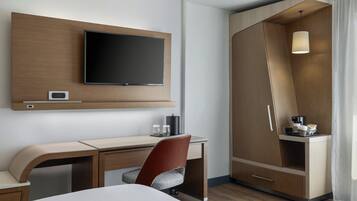 Una habitación de hotel moderna con televisor de pantalla plana, escritorio, silla, armario e iluminación colgante.