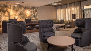 A modern lobby with a seating area featuring armchairs and a sofa, a coffee table, and a large abstract wall art piece.