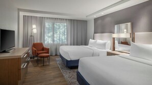A hotel room with two beds, a desk, a chair, a TV, and a large window with curtains.