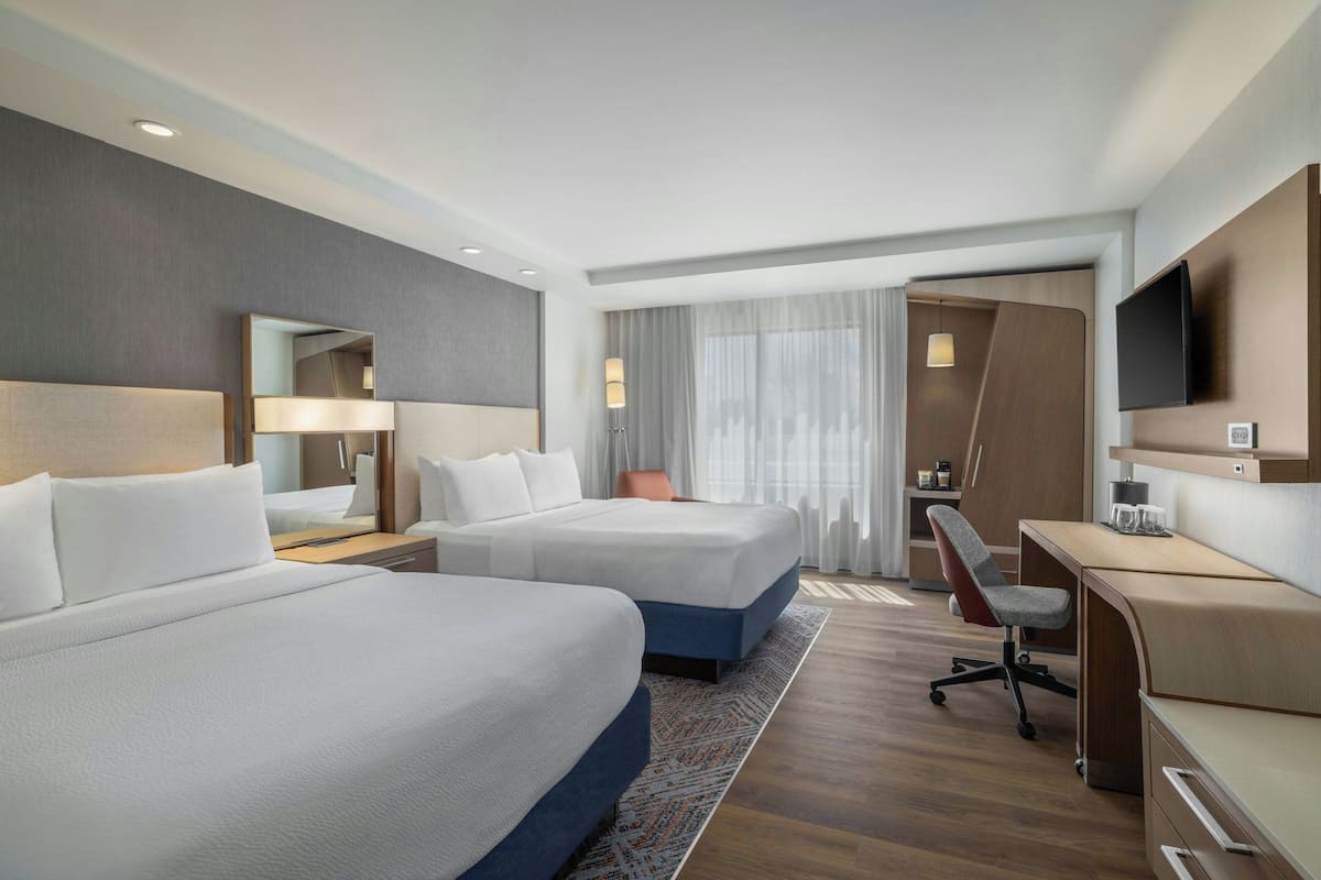 A hotel room with two beds, a desk, a chair, a TV, and a mirror.