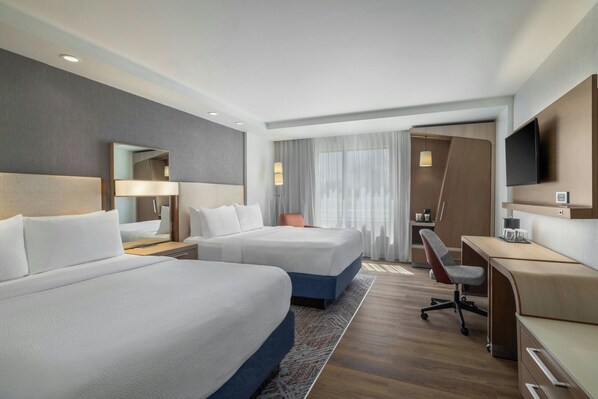Habitación de hotel con dos camas, un escritorio, una silla, un televisor y un espejo.