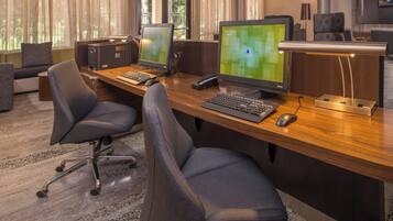 A modern office with two desks, each with a computer monitor, keyboard, and mouse. There are two office chairs, a sofa, and a small table.