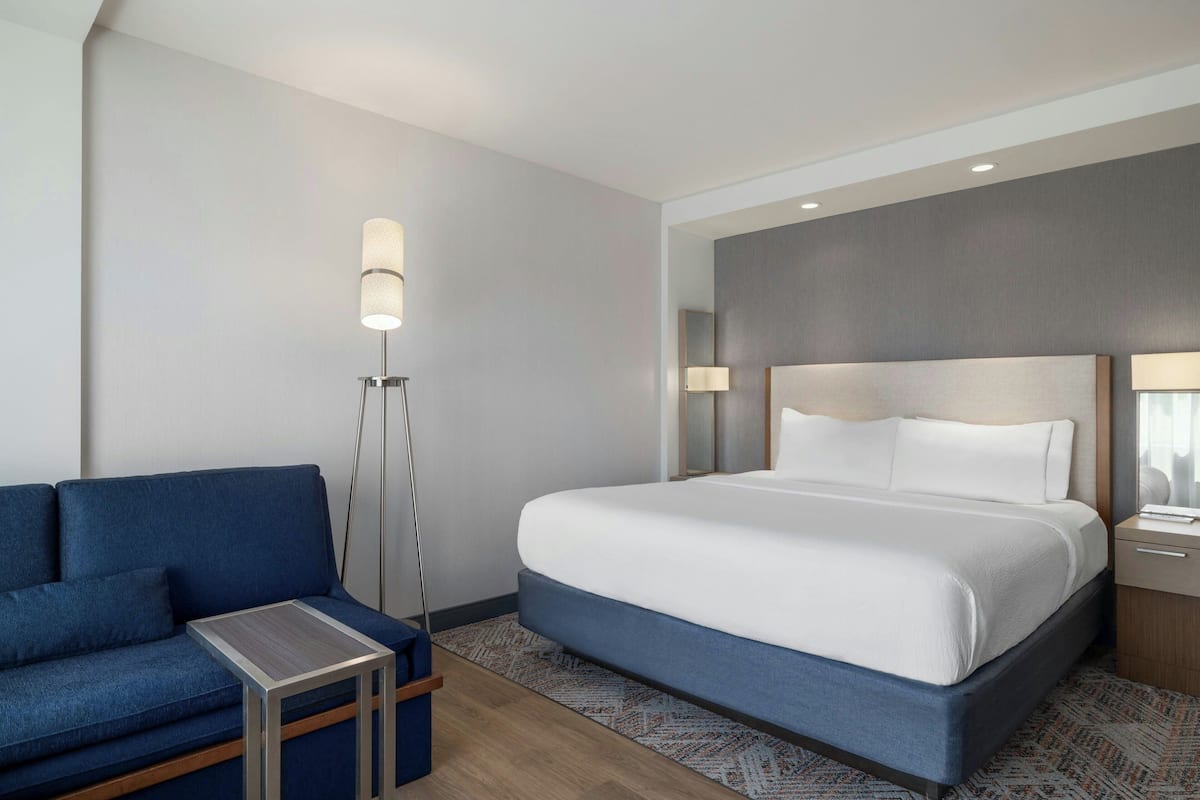 A hotel room with a bed, a sofa, a small table, and a floor lamp.
