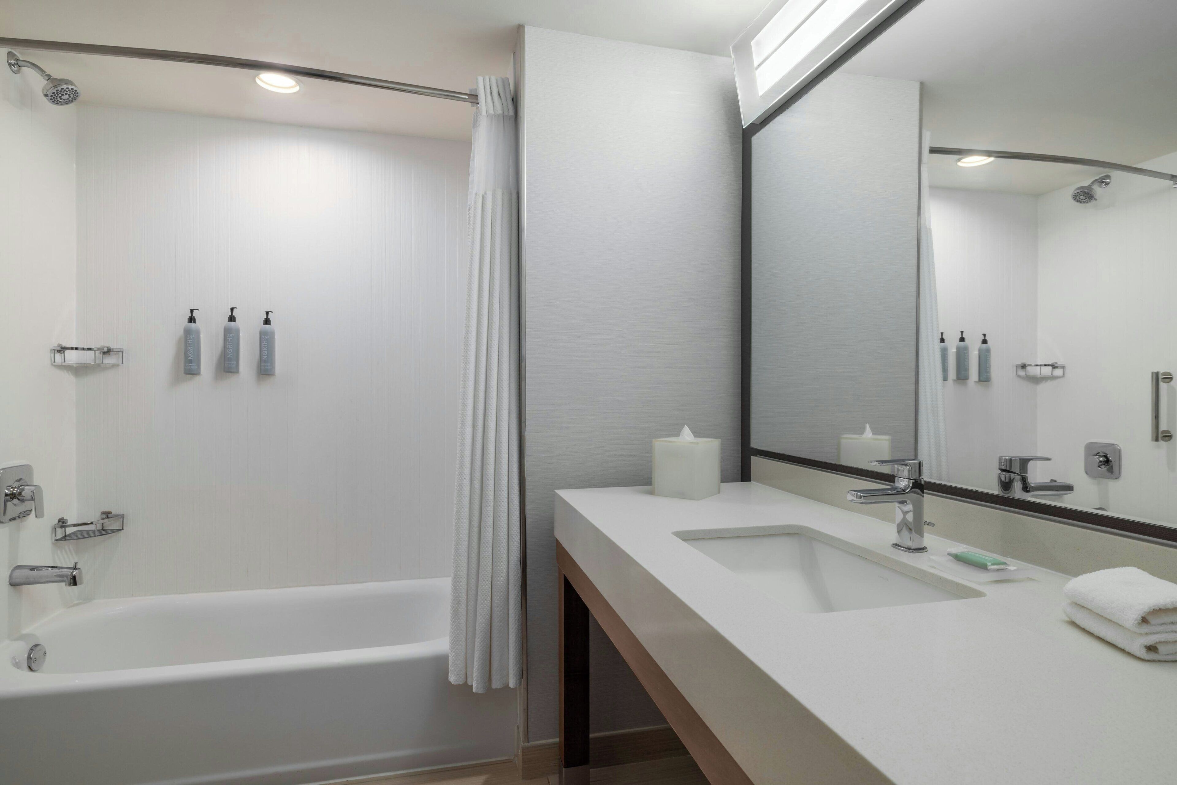 A modern bathroom with a bathtub, a sink, a mirror, and toiletries.