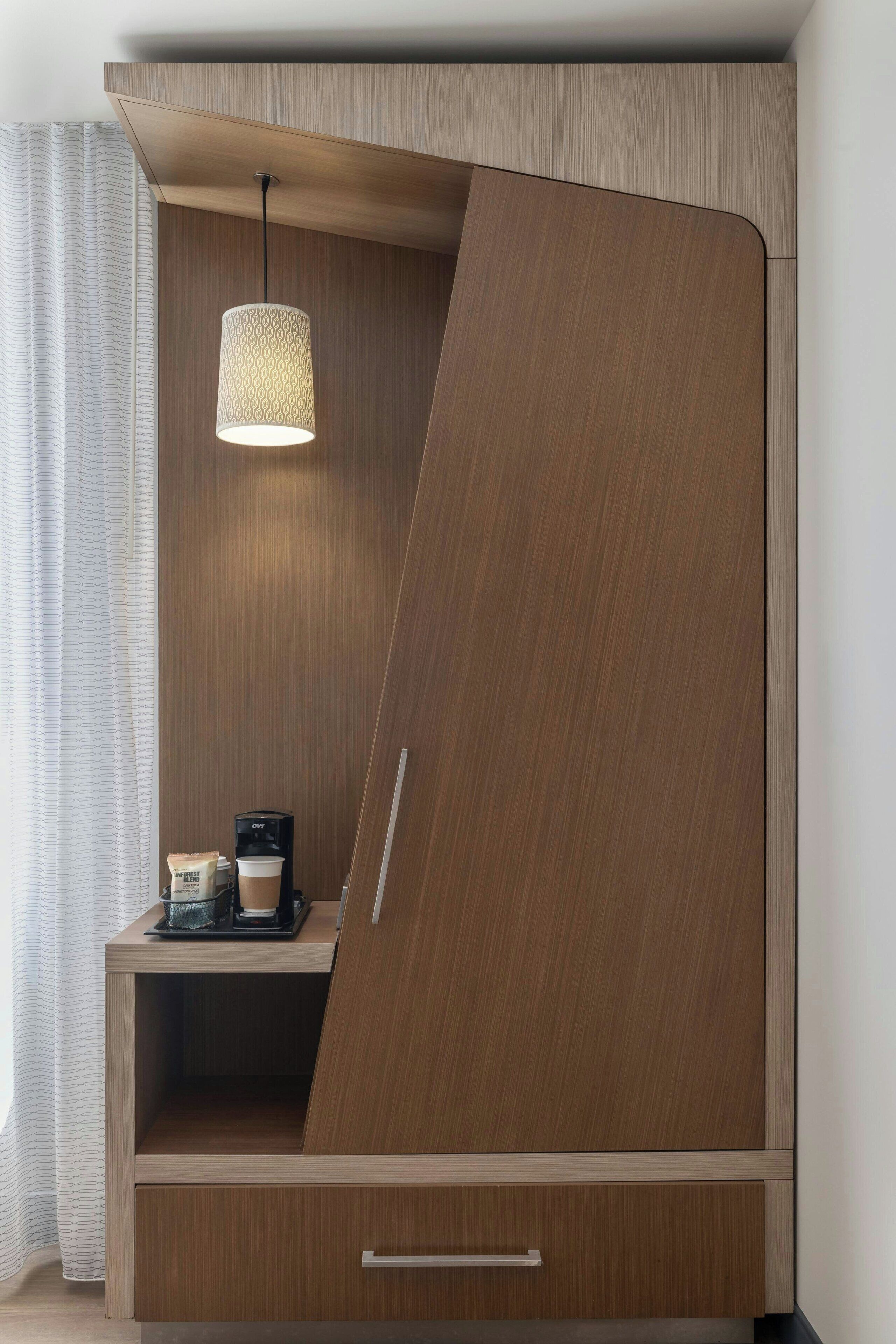 A modern room with a wooden wardrobe, a hanging light fixture, and a coffee machine on a small table.