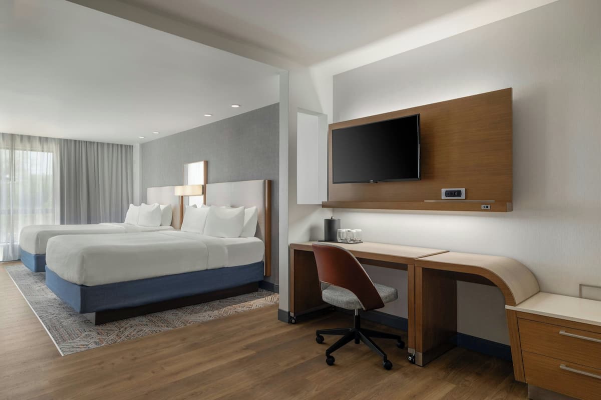 A hotel room with two beds, a desk, a chair, a TV, and a window with curtains.