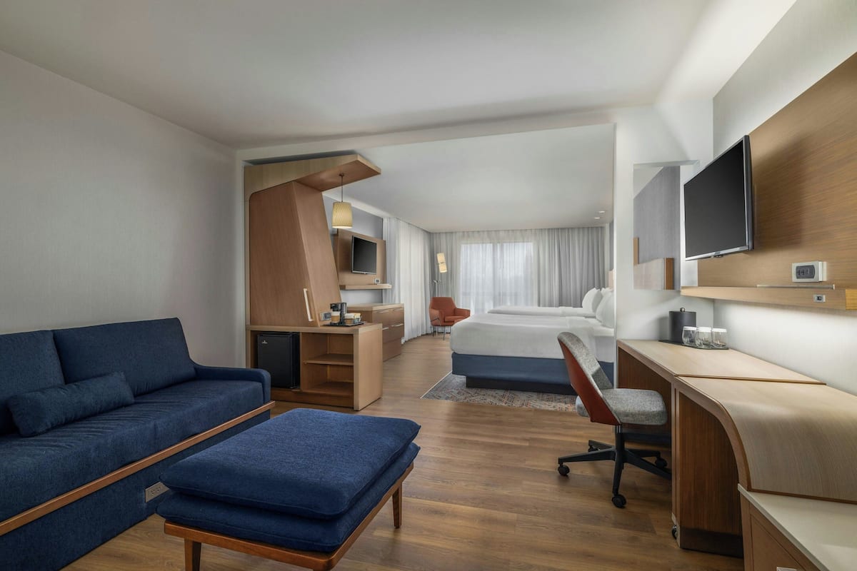 A hotel room with a sofa, a bed, a desk, a chair, a TV, and a TV stand.