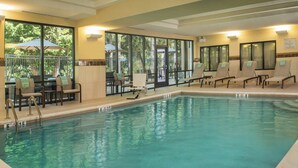 A swimming pool with lounge chairs and umbrellas, surrounded by large windows and doors.