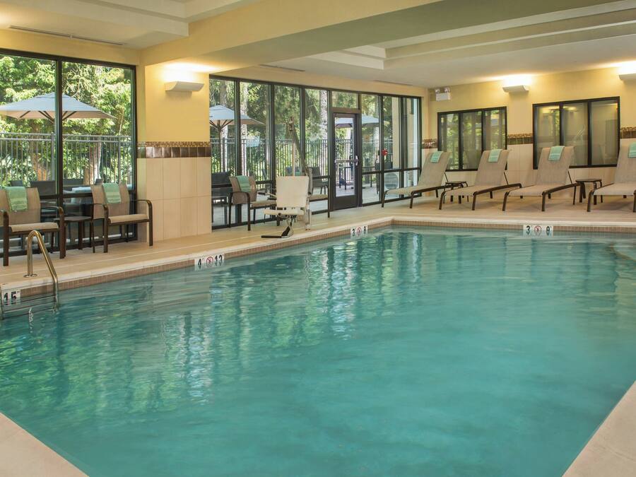 Una piscina con sillones de descanso y sombrillas, rodeada por grandes ventanales y puertas.