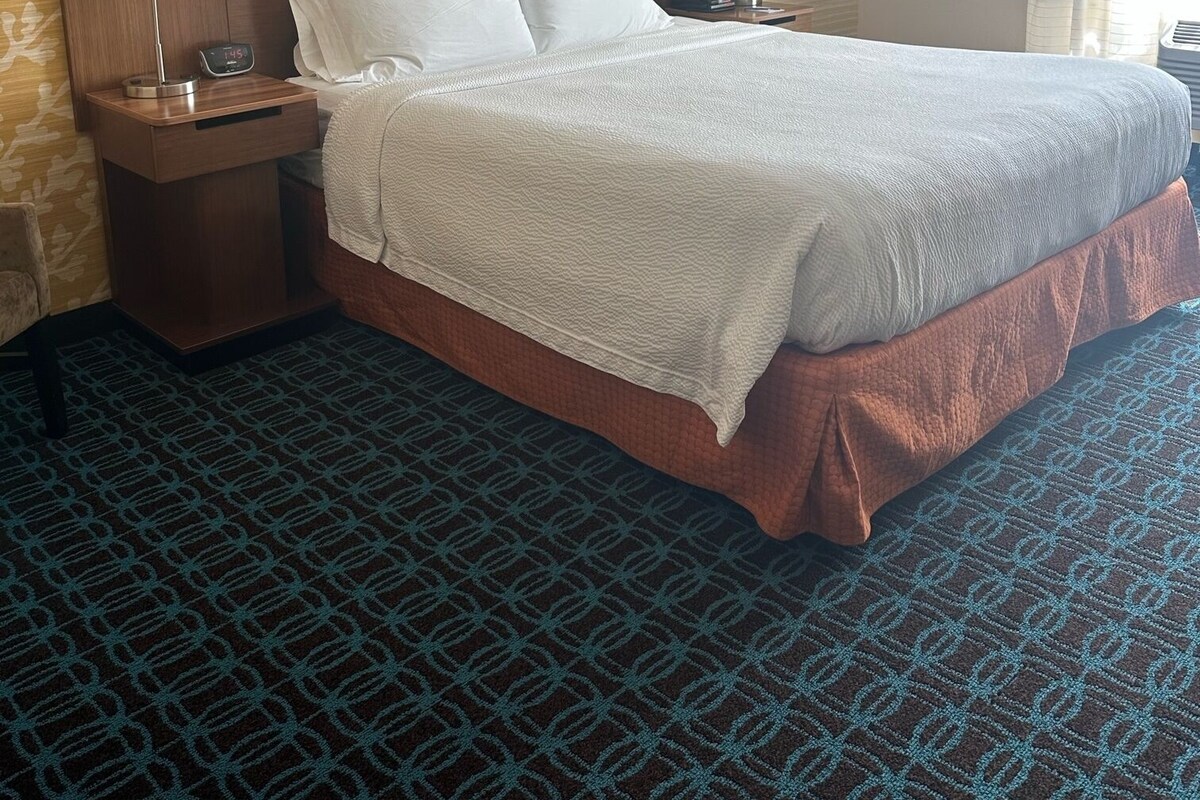Een hotelkamer met een groot bed, twee nachtkastjes, een klok en een raam met gordijnen.