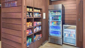 Un mercado de barrio con estantes llenos de aperitivos y una vitrina refrigerada.