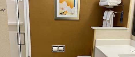 Un baño moderno con cabina de ducha de vidrio, inodoro y lavamanos con toallero.