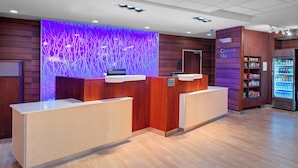 Zona de recepción de un hotel con diseño moderno, que incluye un mostrador de recepción, un letrero que dice 'Corner Market' y un refrigerador con bebidas.