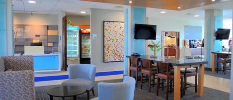 A hotel lobby with seating areas, a coffee bar, and a television.