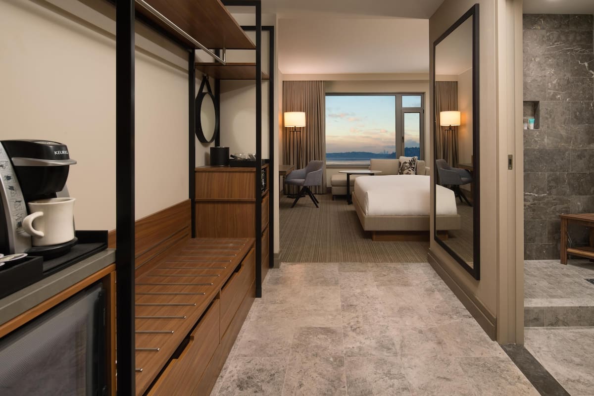 Une chambre d’hôtel comprenant un lit, un bureau avec une machine à café, une chaise, un canapé, un grand miroir et une vue sur le paysage urbain.