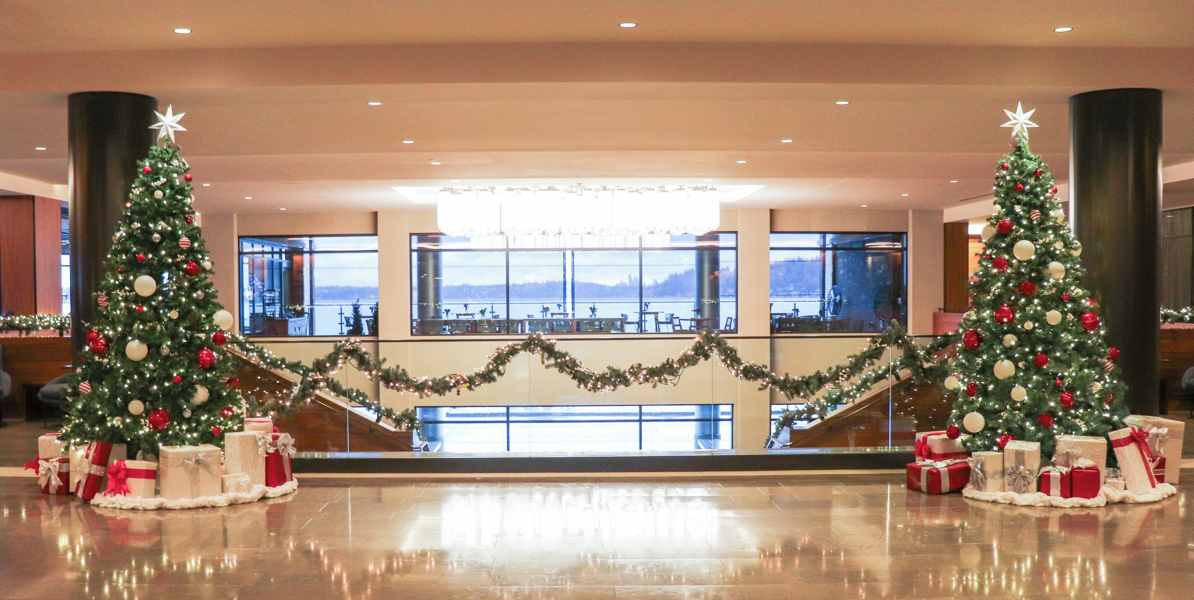 A lobby with two Christmas trees, a view of a lake, and a reflective floor.