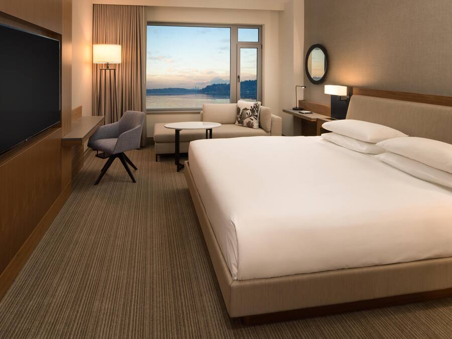 Une chambre d’hôtel avec un grand lit, un bureau, une chaise, une télévision et une fenêtre donnant sur l’eau.
