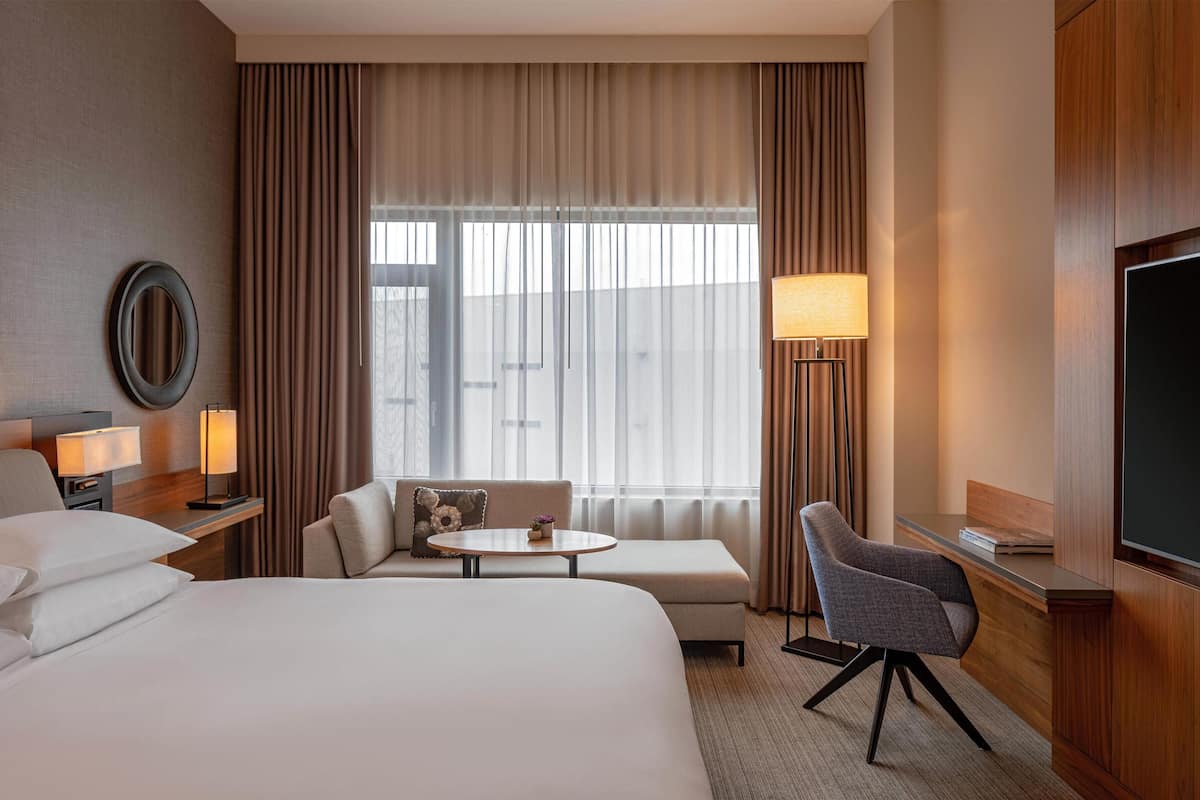 Une chambre d’hôtel avec un lit, un canapé, une petite table, une chaise, une télévision et une fenêtre avec des rideaux.