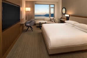 Habitación de hotel con una cama grande, un escritorio, una silla, un televisor y una ventana con vista al agua.