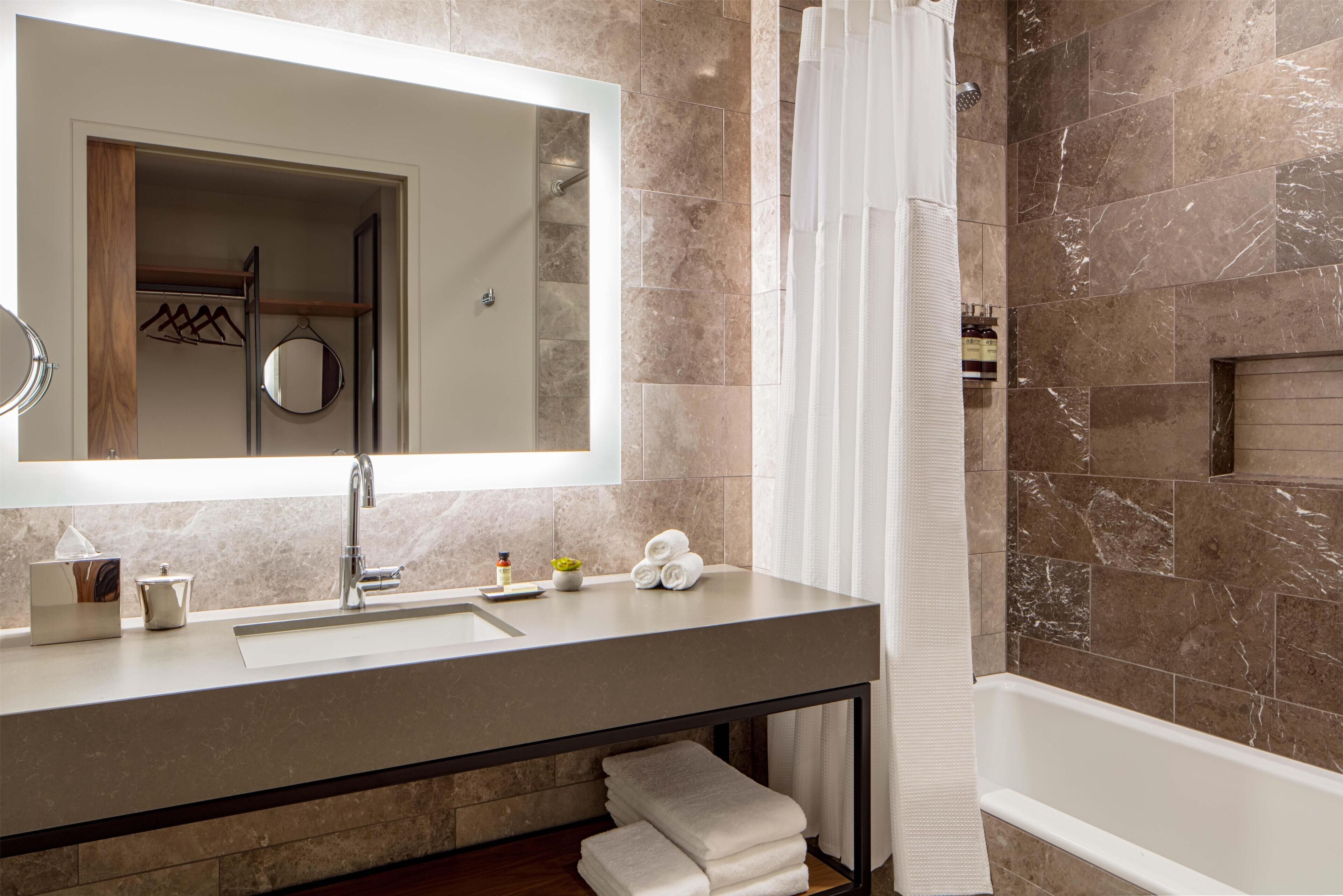 A modern bathroom with a large mirror, a sink, a bathtub, and a shower area.