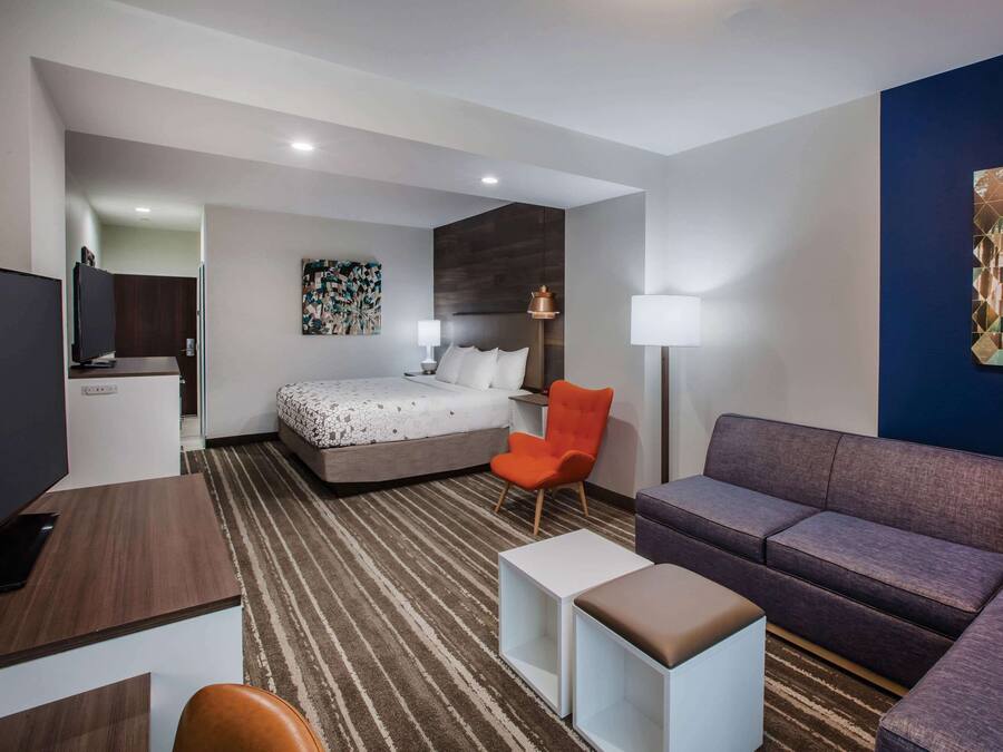 A modern hotel room with a bed, a sofa, a desk, and a TV.