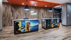 A reception area with wooden panel walls, two reception desks with colorful artwork, and a 'hello sunshine' sign. - La Quinta Inn & Suites by Wyndham Owasso (Owasso)