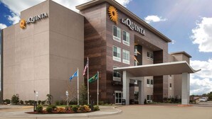 A La Quinta hotel with a modern design, featuring a prominent entrance and a landscaped area with flags. - La Quinta Inn & Suites by Wyndham Owasso (Owasso)