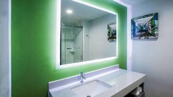 Un baño con un espejo grande, paredes verdes y un lavamanos blanco.