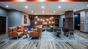 A modern lounge area with sofas, armchairs, and a coffee table, featuring a brick wall and recessed lighting. - La Quinta Inn & Suites by Wyndham Owasso (Owasso)