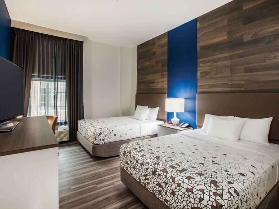 A hotel room with two beds, a desk, a TV, and a window with curtains.