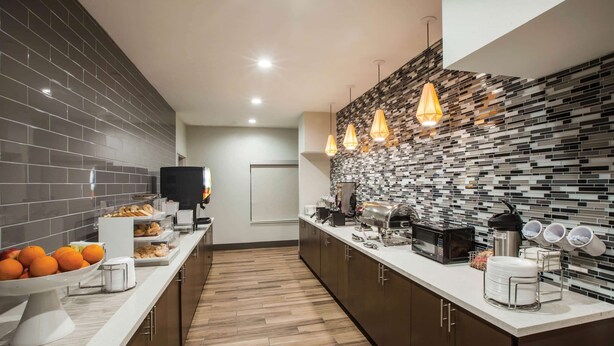 A modern kitchen with a long counter, a tiled backsplash, and hanging pendant lights. - La Quinta Inn & Suites by Wyndham Owasso (Owasso)