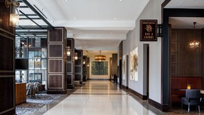 Un hall d’hôtel moderne avec un sol ciré, un comptoir d’accueil et un espace bar/salon.