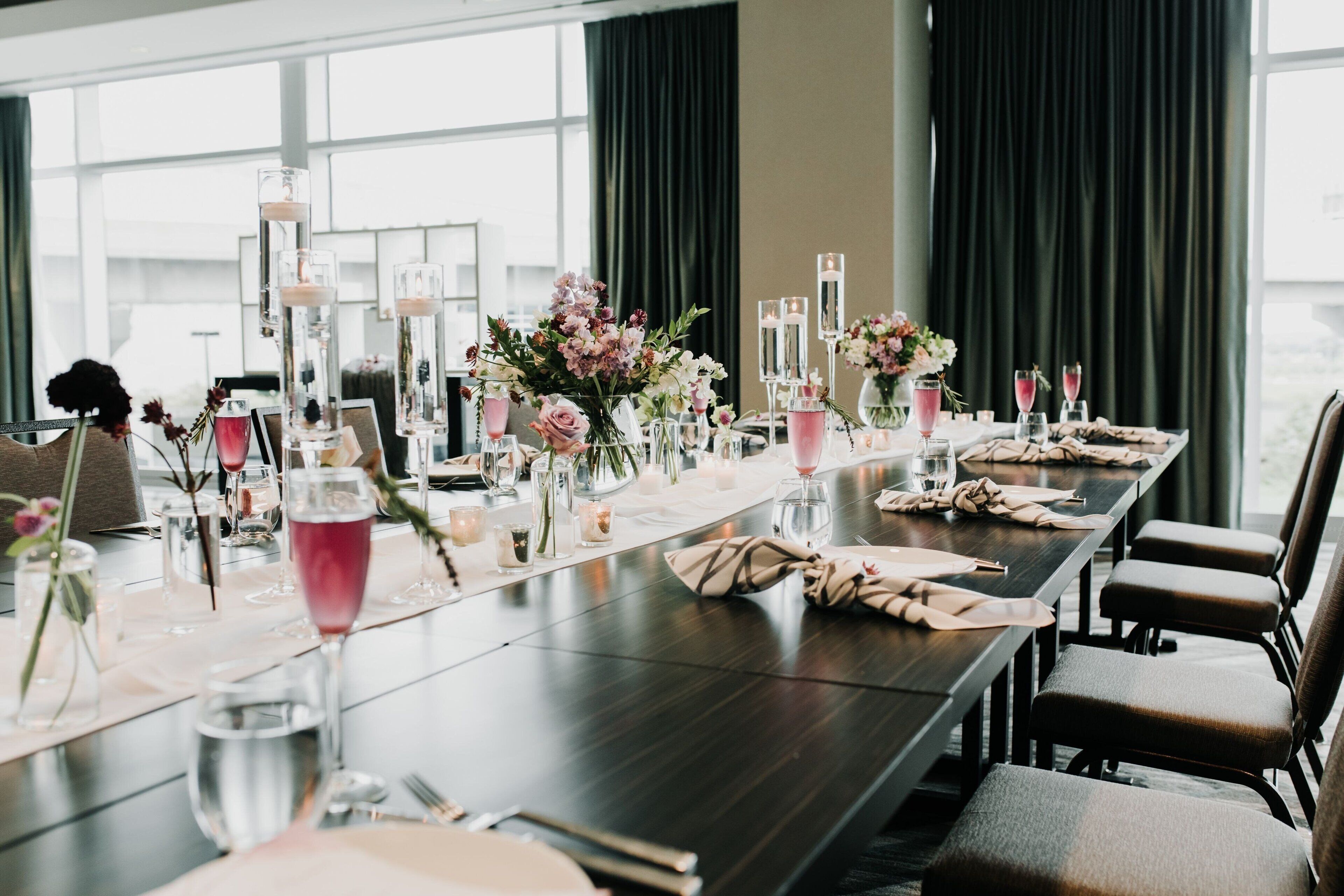 A long dining table set with floral centerpieces, candles, and glasses.