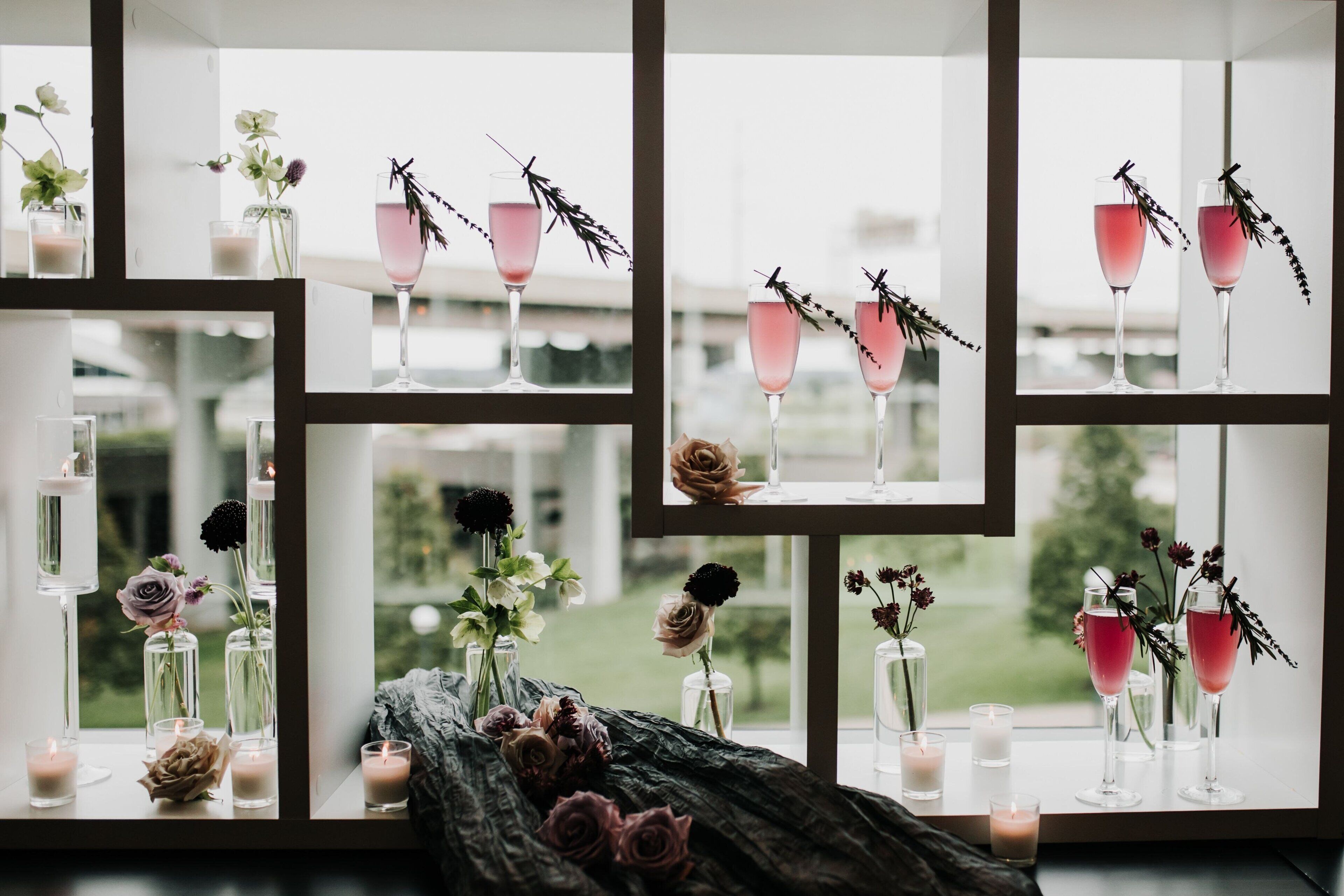 Une pièce dotée de nombreuses fenêtres, chacune présentant une composition différente de vases, de fleurs et de bougies.
