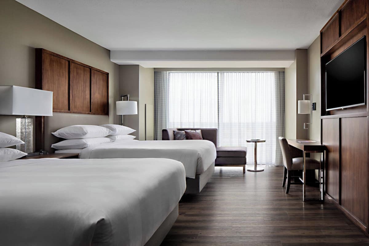 Habitación de hotel con dos camas, un escritorio, una silla, un televisor y una ventana con cortinas.