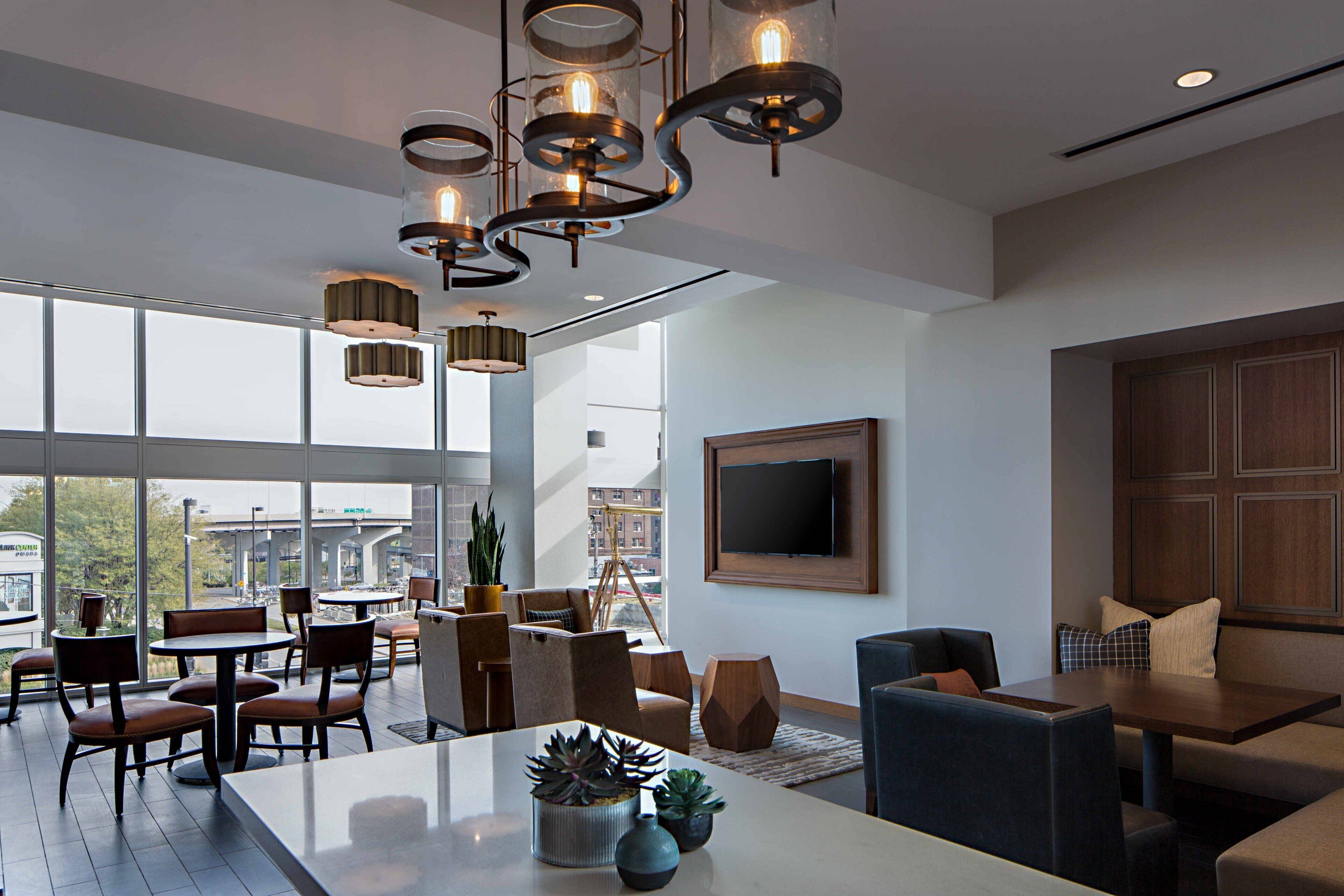 Een moderne hotellobby met een ruim zithoek, een eettafel en een aan de muur bevestigde televisie.