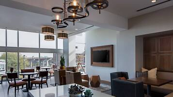 Een moderne hotellobby met een ruim zithoek, een eettafel en een aan de muur bevestigde televisie.