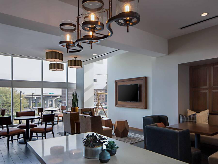 Een moderne hotellobby met een ruim zithoek, een eettafel en een aan de muur bevestigde televisie.
